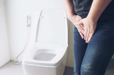 Woman touching her lower belly next to a toilet.