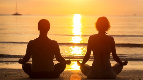 Couple meditating at a beach during sunset