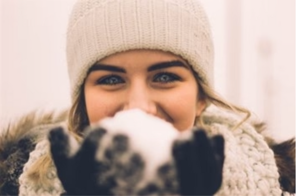 Woman holding a snow ball next to her face.