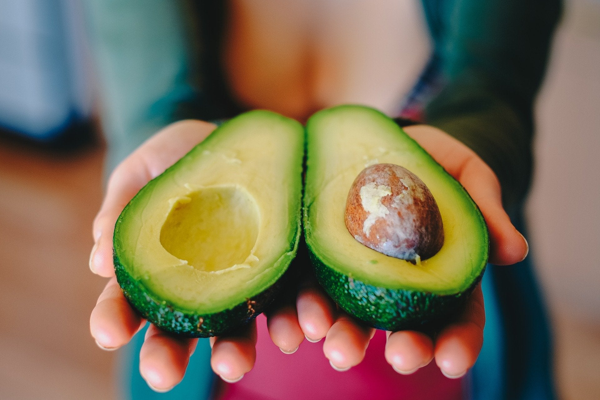 Woman holding avocado halves.