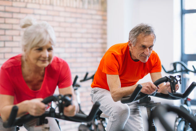 Senior couple cycling on exercise bikes.