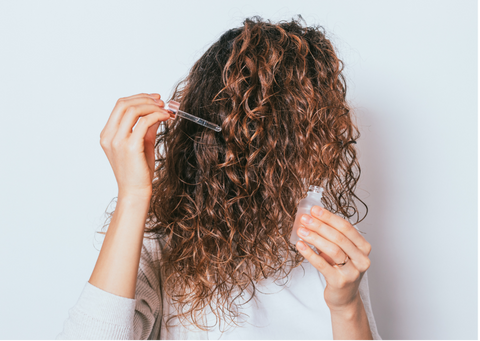 Woman applying drops of oil to her hair.