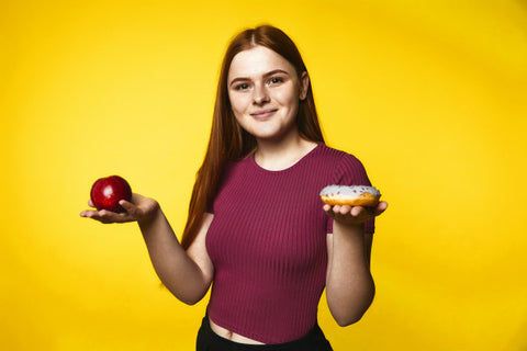 Woman holding an apple in one hand and a donut in the other.