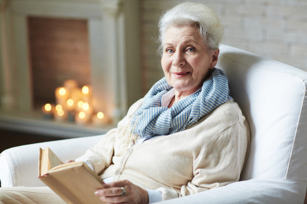 Senior woman reding a book on the couch.