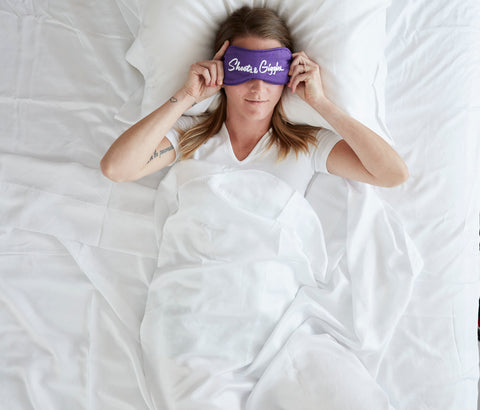 Woman adjusting purple eye mask in bed