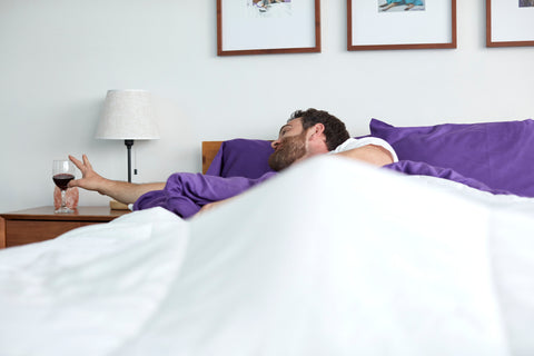 man in bed reaching for a glass of red wine