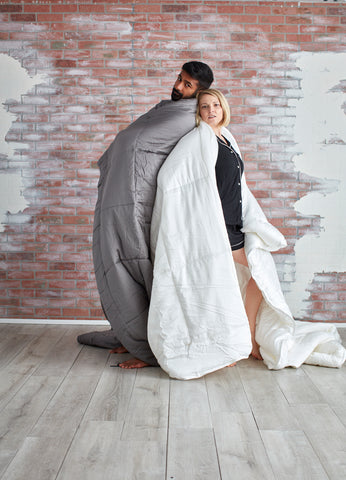 a couple standing back to back with comforters over their shoulders