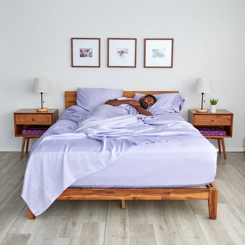 a man asleep in a bed with lavender sheets