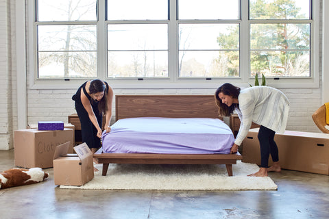 Two women putting a bottom sheet on a mattress