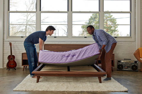 Two men setting up a mattress on a bed frame