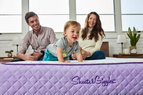 Two parents and a baby sitting on a mattress