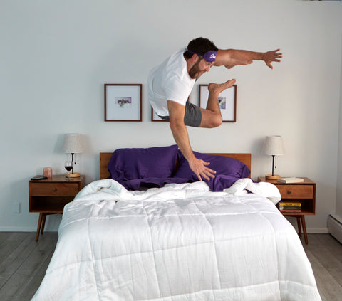 Man jumping over bed with white comforter