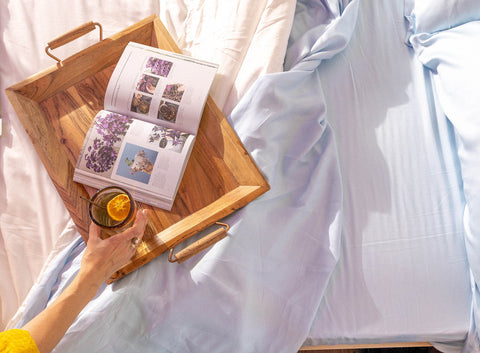 a hand grabbing a glass of water on a wooden tray on a bed