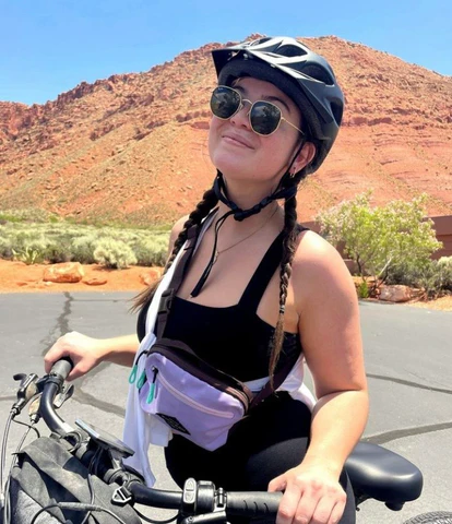 Sherpani staff member smiles at the camera from atop her mountain bike in St. George, Utah. She is wearing Sherpani hip pack, the Hyk in Lavender as a small crossbody.