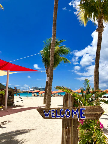 A white beach with palm trees and "Welcome" sign on the island of St Martin in the Caribbean