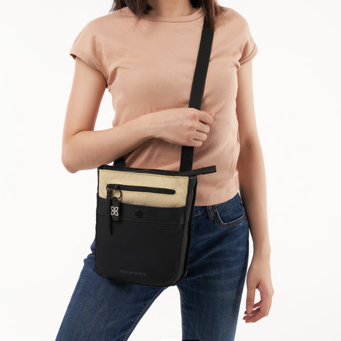 A model wearing Sherpani minimalist crossbody Anti-Theft bag, the Prima in Straw