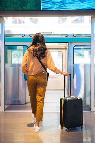A woman with her Sherpani suitcase, the Meridian in Chromatic, stepping onto an airport train