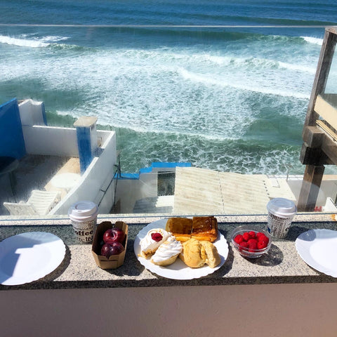 A breakfast spread of pastry, fruit and coffee sitting outside on a deck with an ocean view in Ericeira, Portugal