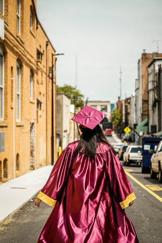A woman walks down a street in her graduation cap and gown