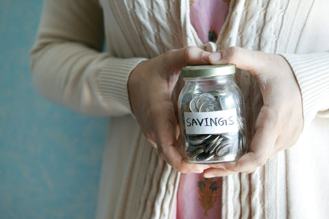 A woman holding a jar full of change that is labeled "savings"