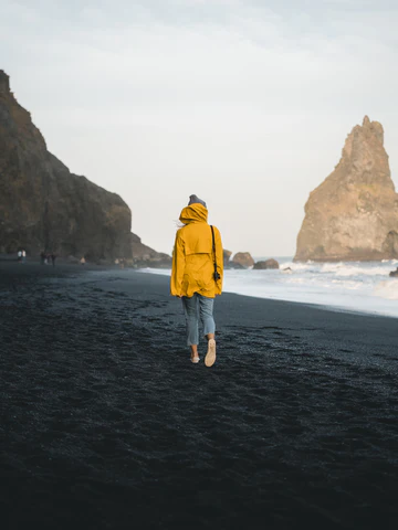 A woman walking on the beach in gloomy weather, wearing a bright yellow raincoat