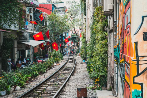 Train tracks run through an alley with brightly colored walls and many Vietnamese flags