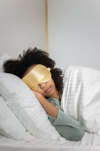 A black woman in bed with an eye mask on