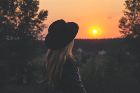 A woman wearing a hat turns to face the setting sun