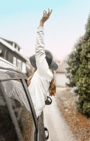 A woman reaches toward the sky out the passenger window of a car