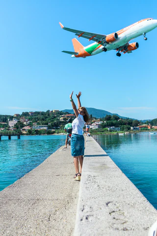 A woman stands with her hands in the air as a plane flies overhead.