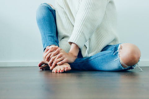A woman sits on the ground with her hands and feet visible