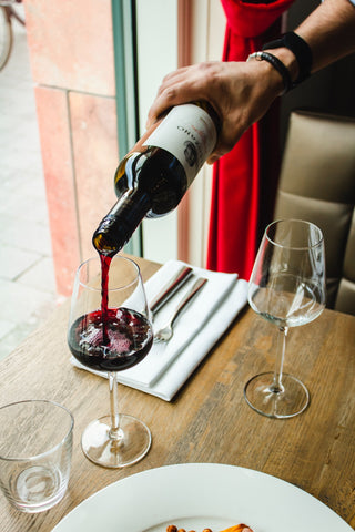 A server's hand pouring red wine into a glass