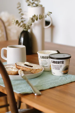 A Montreal style bagel sitting on a table alongside cream cheese and a cup of coffee