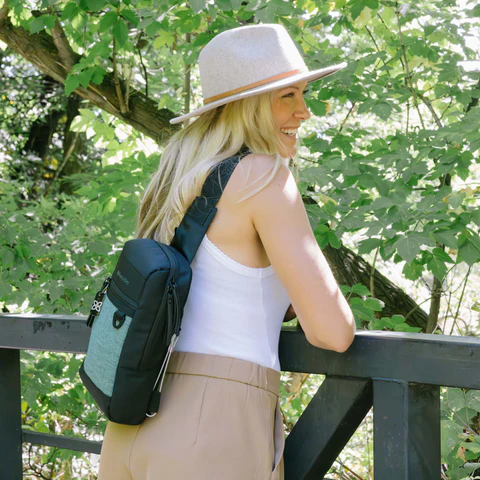 A woman leans on a railing outside wearing the Metro mini travel sling.