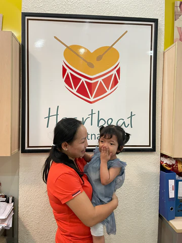 A Vietnamese mother holding her young daughter in front of Heartbeat Vietnam logo.