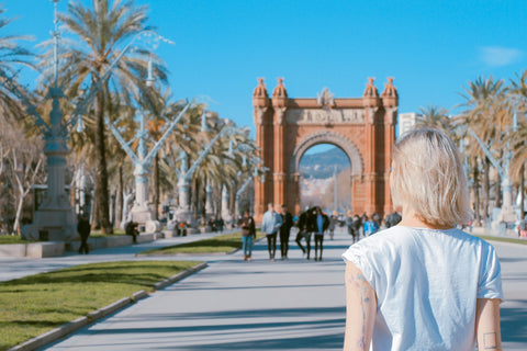 A blonde woman facing away from the camera is looking at a view of architecture and palm trees in Spain