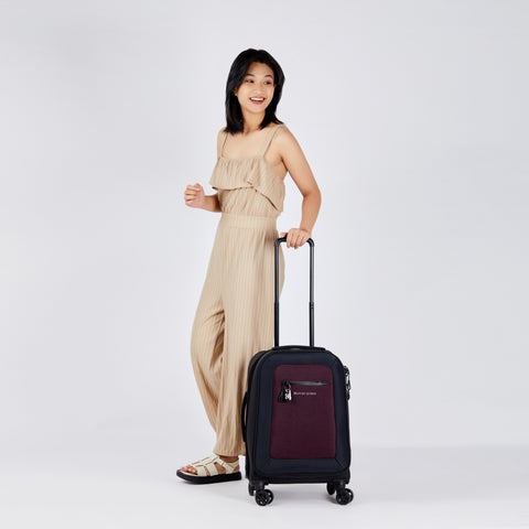 A woman standing and holding the handle of Sherpani carry-on suitcase the Latitude.