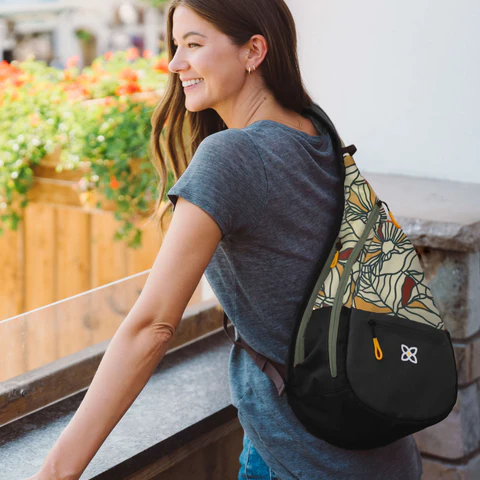 A woman standing on an outdoor balcony. She is wearing Sherpani sling backpack, the Esprit