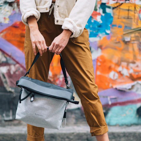 A woman standing in front of a colorful wall. She is carrying Sherpani reversible travel bag, the Vale