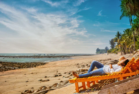 A woman lounges on a beach chair with her hat pulled over her eyes