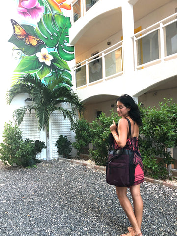 A woman standing in front of a colorful mural with her Sherpani convertible travel bag, the Soleil (Merlot color)