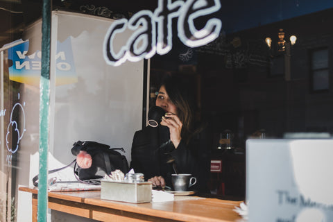 A dark haired woman sipping coffee through a cafe window