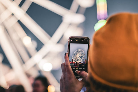 A woman takes a photo of a ferris wheel with her phone.