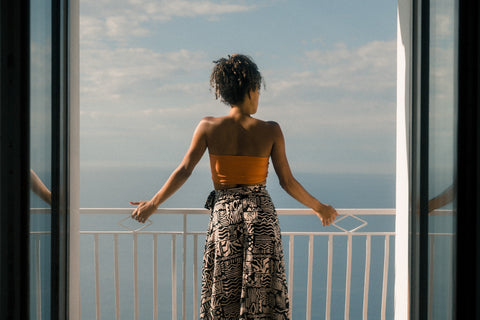 A woman with curly hair stands on a scenic balcony overlooking water.