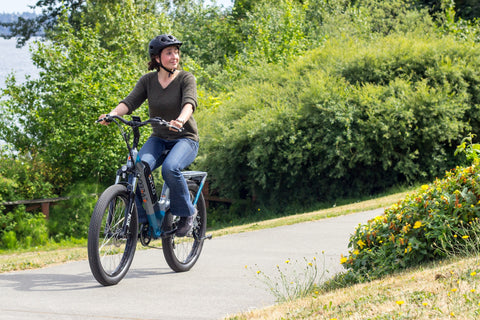 A smiling woman rides a bicycle down a scenic path.