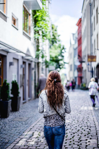 A woman with long brown hair walks down a cobblestone street.