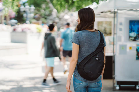 A woman facing away from the camera is wearing Sherpani Anti-Theft sling backpack, the Esprit AT