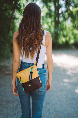 A woman walking away from the camera on a path, she is wearing Sherpani crossbody travel bag, the Sadie