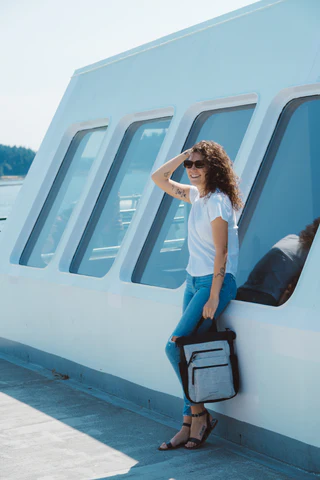 A woman leans against an outdoor wall, she carries Sherpani Anti-Theft bag, the Soleil