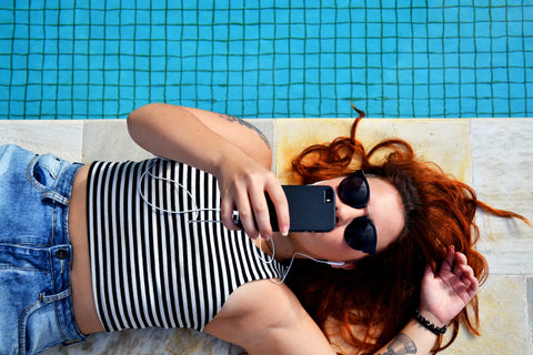A woman lays by the pool looking at her phone